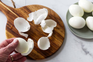Hand peeling a hard-boiled egg with discarded shells on a board.