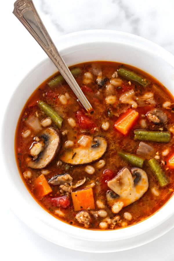 Vegetable barley soup in a bowl with a silver spoon.