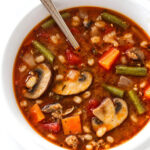 Vegetable and mushroom soup in a bowl with a metal spoon.