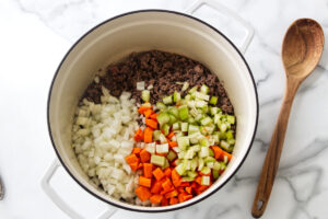 Ground meat, onions, carrots, and celery cooking in a white pot.