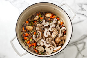 Sliced mushrooms, carrots, celery, and ground meat cooking in a pot.