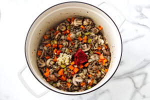 Dutch oven with sautéed meat, carrots, mushrooms, garlic, and paste.