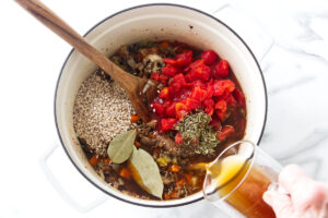 Pouring broth into soup ingredients using a wooden spoon.