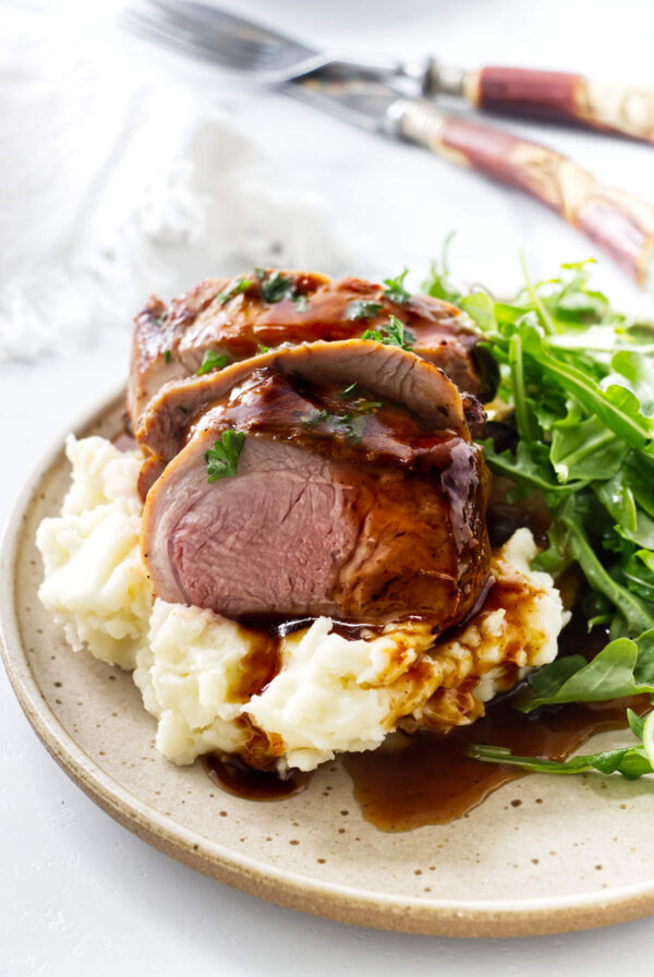 Sliced roast pork with gravy, mashed potatoes, and arugula.