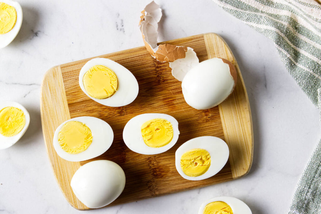 Hard-boiled eggs, some halved, resting on a wooden cutting board.