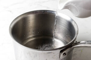 Water pouring from a pitcher into a stainless steel saucepan.