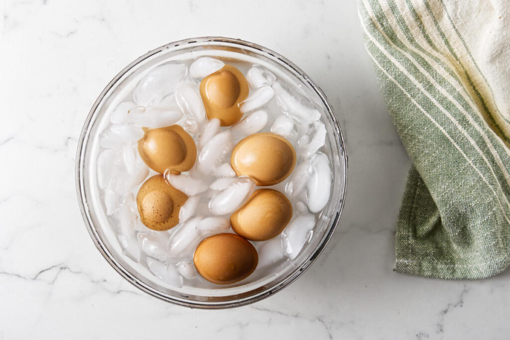 Brown eggs in a glass bowl with ice and water.