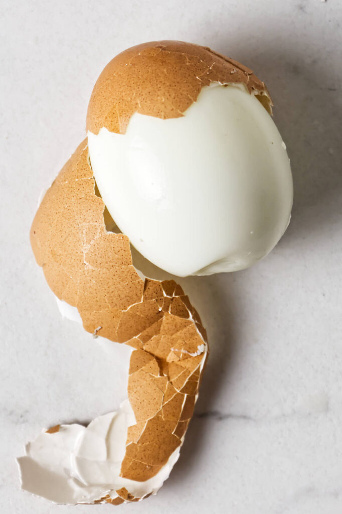 A peeled steam cooked hard-boiled egg with cracked brown shell fragments.