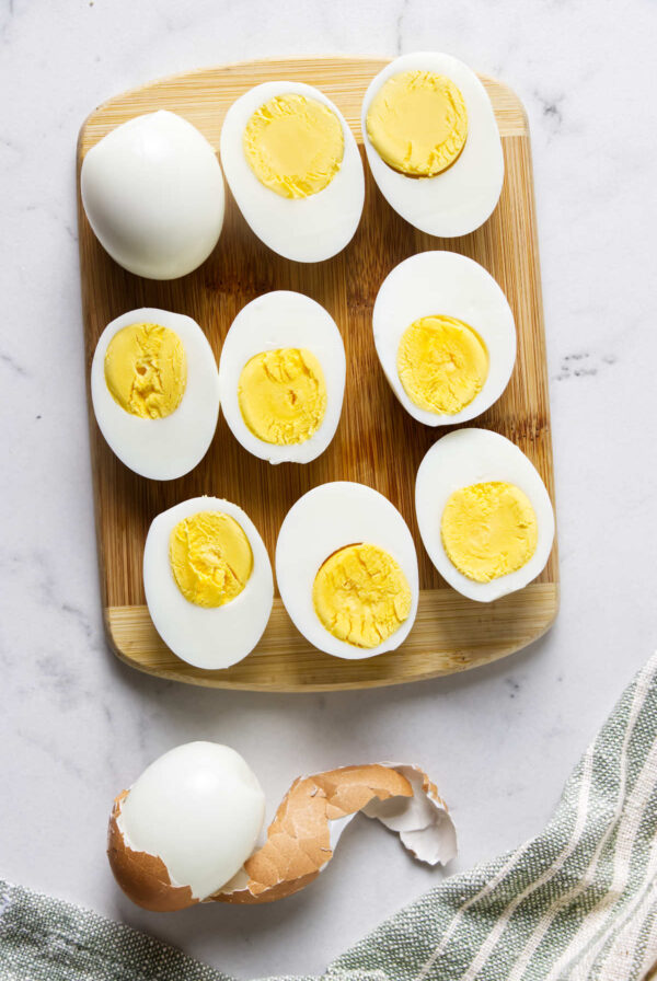 Halved and whole hard-boiled eggs on a wooden cutting board.