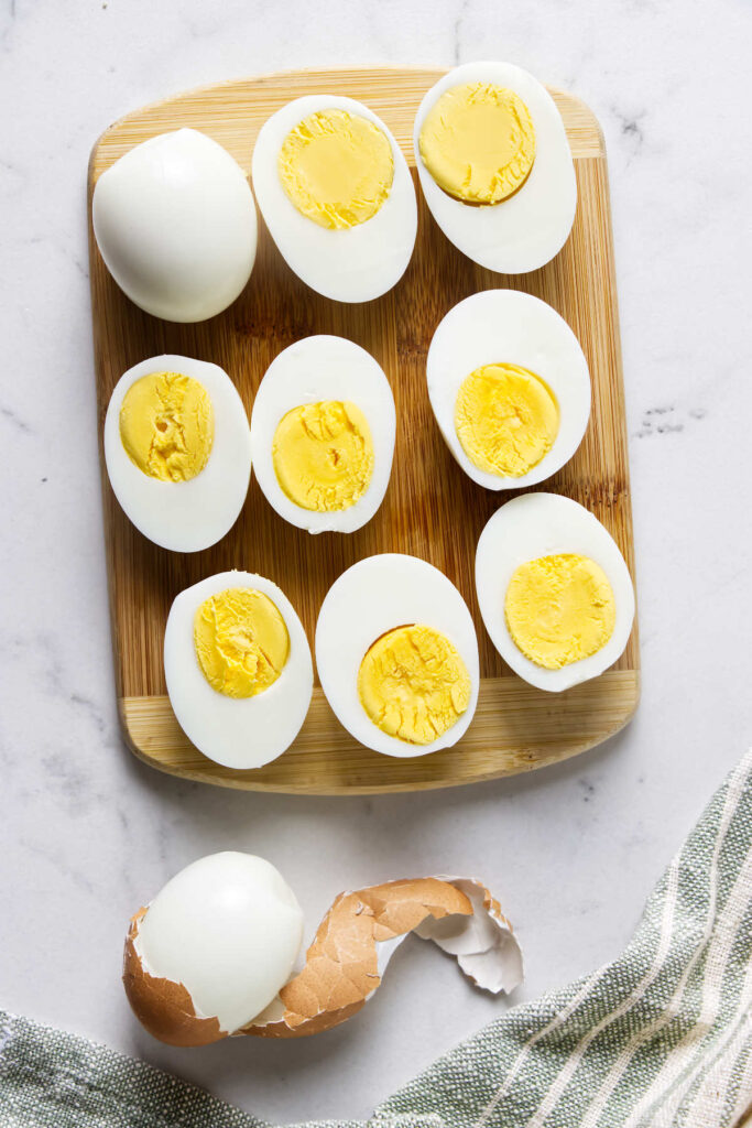 Halved and whole hard-boiled eggs on a wooden cutting board.